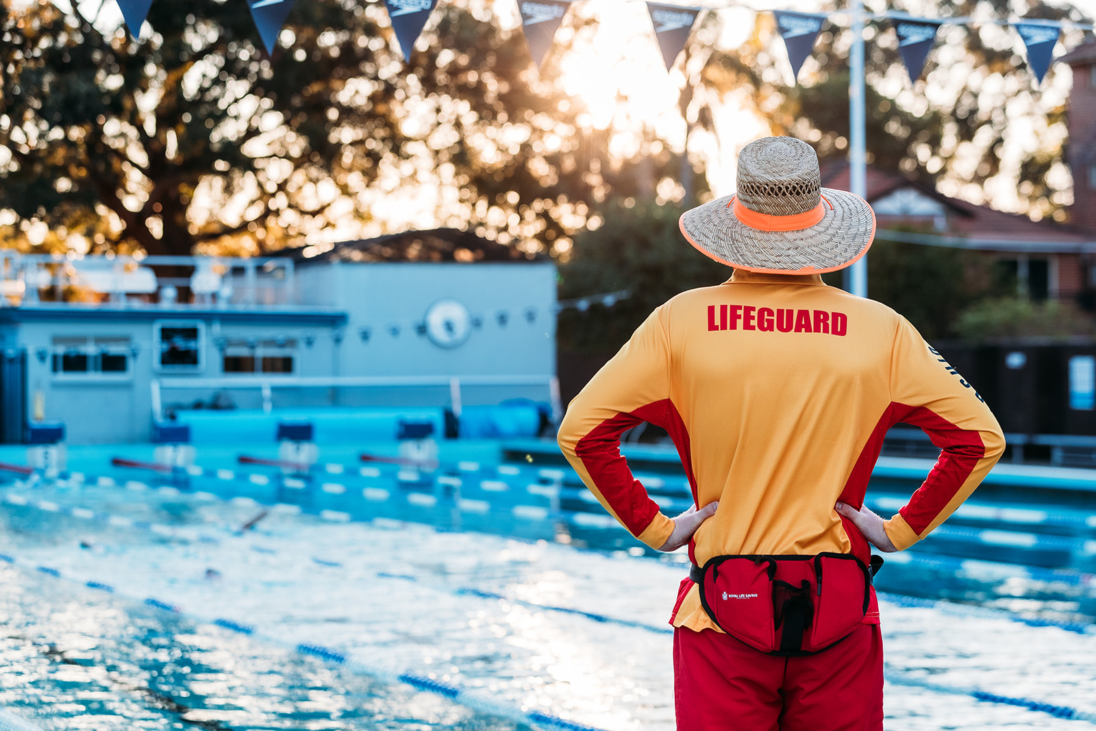 The back of a lifeguard from the waist up wearing a straw hat